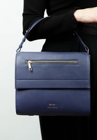 Donkerblauwe textuur leren handtas met een bovenhandvat, een voorzak met rits en gouden hardwareaccenten. Glad oppervlak met een modern, gestructureerd ontwerp.