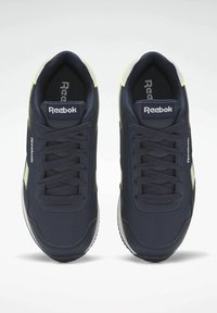 Mörkblå sportskor i texturerat syntetmaterial med kontrasterande gula detaljer och vita gummisulor. Har snören och varumärkesdetaljer.