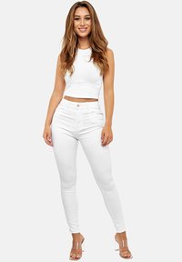 Top corto blanco combinado con jeans ajustados blancos. El conjunto presenta una textura suave y se complementa con sandalias de tacón alto transparentes.