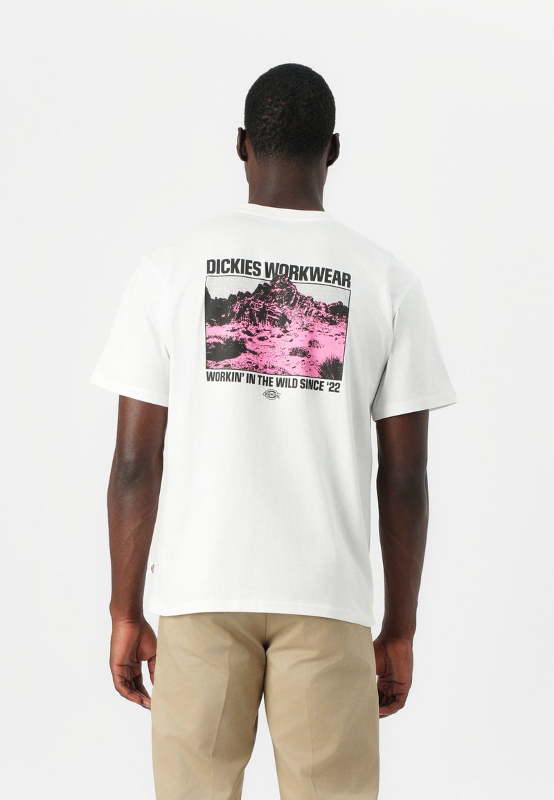 Camiseta blanca de algodón con un estampado gráfico de montañas en negro y rosa en la parte posterior, con el texto "DICKIES WORKWEAR" arriba.