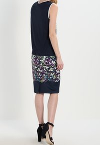 Šaty bez rukávů s jednolitým námořnickým vrškem a spodní částí s květinovým vzorem v odstínech fialové, zelené a modré; do šatů ke kolenům s přiléhavým stylem.