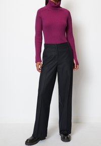 Fitted ribbed turtleneck in deep purple paired with wide-leg black trousers. Black ankle boots with a textured sole complete the look.