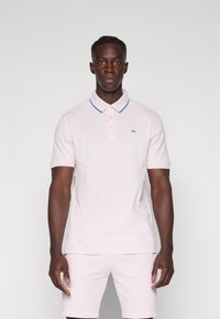 Polo shirt rosa claro com um acabamento azul na gola e uma pala com três botões. Apresenta um pequeno logótipo bordado no lado esquerdo do peito.