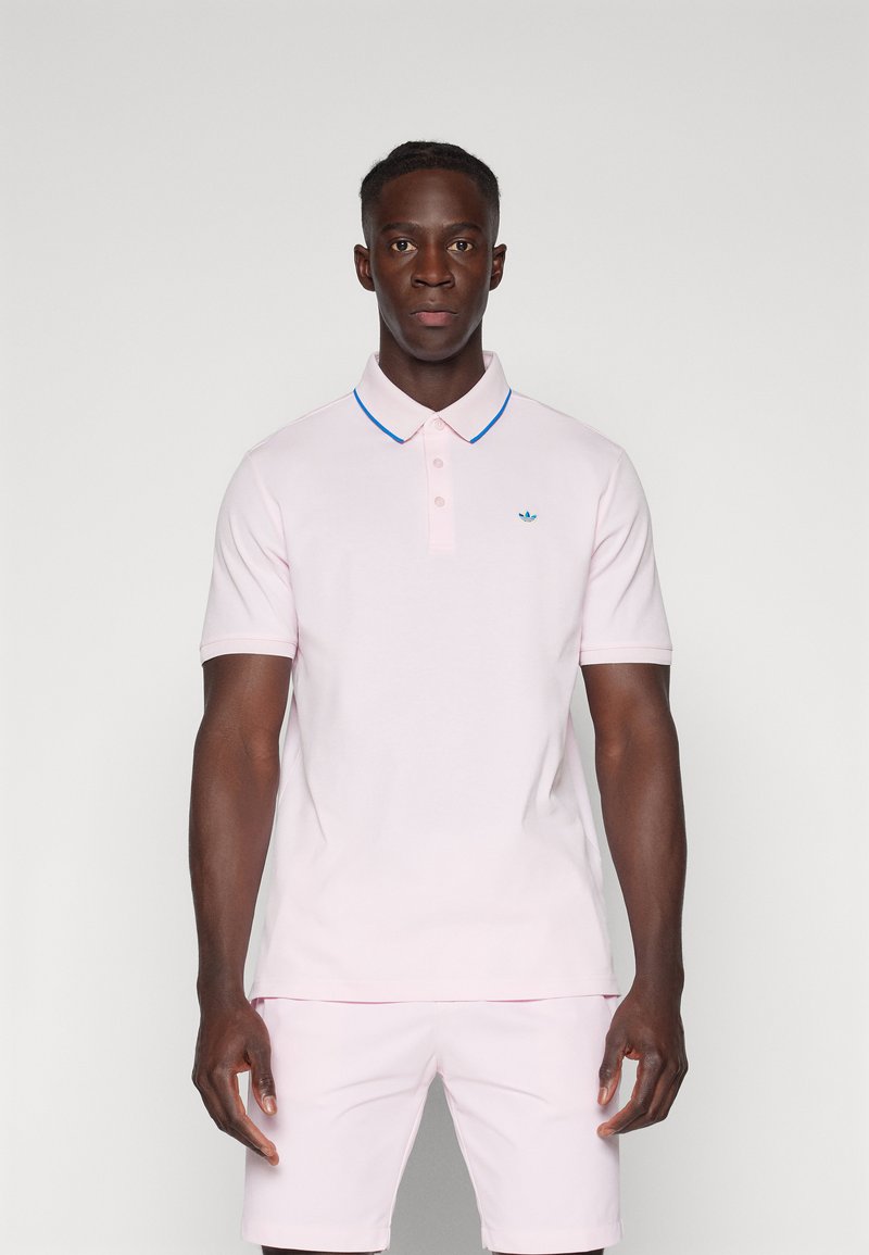 Polo shirt rosa claro com um acabamento azul na gola e uma pala com três botões. Apresenta um pequeno logótipo bordado no lado esquerdo do peito.