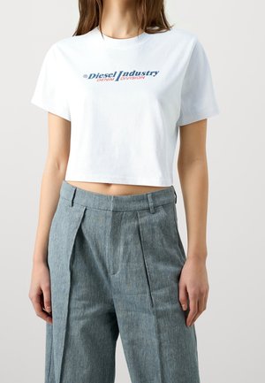 Vrouw die een wit cropped t-shirt draagt met de tekst "Diesel Industry Denim Division" en een hoge grijze geplooide broek.