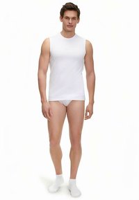 Witte mouwloze tanktop van zachte stof, aansluitend model, gecombineerd met witte slips en sokken, staand tegen een effen achtergrond.
