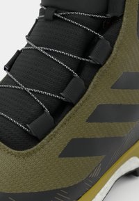 Zielono-czarne buty sportowe z teksturowanej tkaniny, dekoracyjnymi akcentami i solidnym systemem sznurowania. Posiadają trwałą podeszwę i wzmocnione obszary.