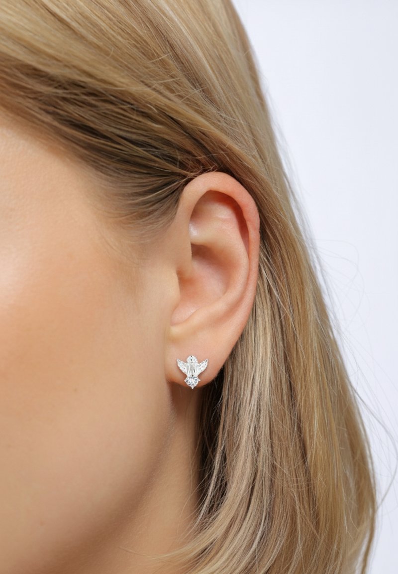 Boucles d'oreilles argentées en forme d'oiseau avec des ailes détaillées, ornées d'un accent en diamant central. Texture métallique lisse.