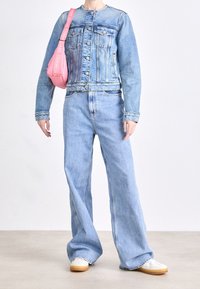 Chaqueta vaquera azul claro con cuello redondo, bolsillos delanteros, combinada con pantalones vaqueros azul claro de pierna ancha y un bolso de hombro rosa. Zapatillas blancas.