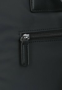 Primer plano de un bolso negro con una superficie texturizada, acento de cuero suave y una cremallera con un tirador rectangular.