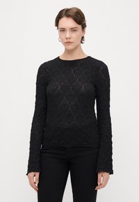 Czarna bluzka z długim rękawem o teksturowanym kwiatowym wzorze, okrągłym dekolcie i rozszerzanych rękawach. Materiał wydaje się lekki, z lekko przezroczystą jakością.