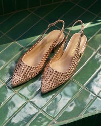 Ζευγάρι μπεζ γόβες slingback με κυκλικό σχέδιο κοψίματος σε λαμπερά πράσινα τετράγωνα πλακάκια κάτω από απαλό φως.