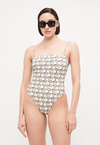 Swimsuit with a square neckline, thin adjustable straps, featuring a multi-colored floral pattern on a cream background.