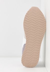 Suola della scarpa con una base in gomma beige strutturata, caratterizzata da un motivo a zigzag, che mostra un design superiore in bianco, grigio chiaro e viola.