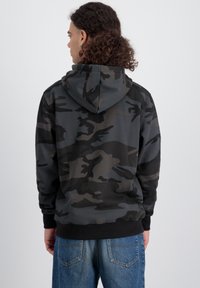 Hoodie u tamnom kamuflažnom uzorku, s opuštenim krojem, rebrastim manžetama i rubom, izrađen od mekog materijala s glatkom teksturom.