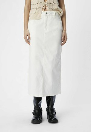 Jupe midi en denim blanc avec fermeture à boutons sur le devant et poches latérales, associée à des bottes noires montantes avec des accents à boucle.
