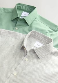 Deux chemises pour hommes pliées à boutons, une vert clair uni et une beige clair avec de fines rayures blanches, toutes deux avec des cols pointus.