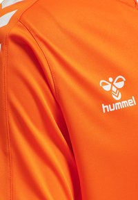 Fel oranje sportstof met wit hummel-logo en chevronstrepen op de schoudernaad.