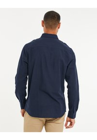 Camisa azul marino de botones con mangas largas, vista trasera. Presenta un cuello clásico, bajo recto y una textura de tela suave.