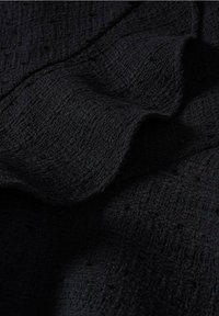 Texturiertes schwarzes Gewebe mit einem gewebten Muster, das subtile Wellen und unterschiedliche Oberflächentiefe aufweist, was visuelles Interesse und Tiefe schafft.