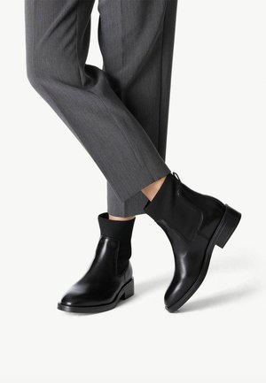 Černé kožené kotníkové boty s elastickými postranními panely a texturovanou tkaninou, doplněné o šedé kraťasy, které vytvářejí elegantní siluetu.