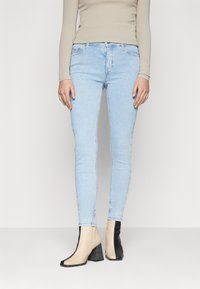 Vaqueros ajustados de color azul claro con una textura suave, con una cintura de altura media y un sutil desvanecimiento. Combinados con botines de dos tonos.