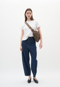 T-shirt bianco a girocollo, jeans a vita alta in denim scuro a gamba larga e borsa a tracolla marrone con texture. Le scarpe ballet flats nere a punta completano il look.