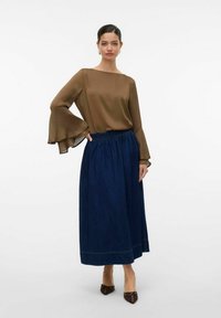 Brun, flödande blus med trumpetärmar, i kombination med en lång, mörkblå denimkjol med elastisk midja och sömdetaljer.