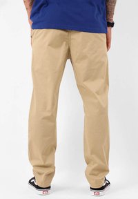 Chinos beige avec une coupe décontractée, en tissu coton. Dotés de passants de ceinture et de poches arrière. Associés à des baskets noires.