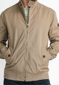 Khaki bomber jacket with a zippered front, ribbed cuffs and hem, two side pockets, and a stand collar. Features smooth, textured fabric.