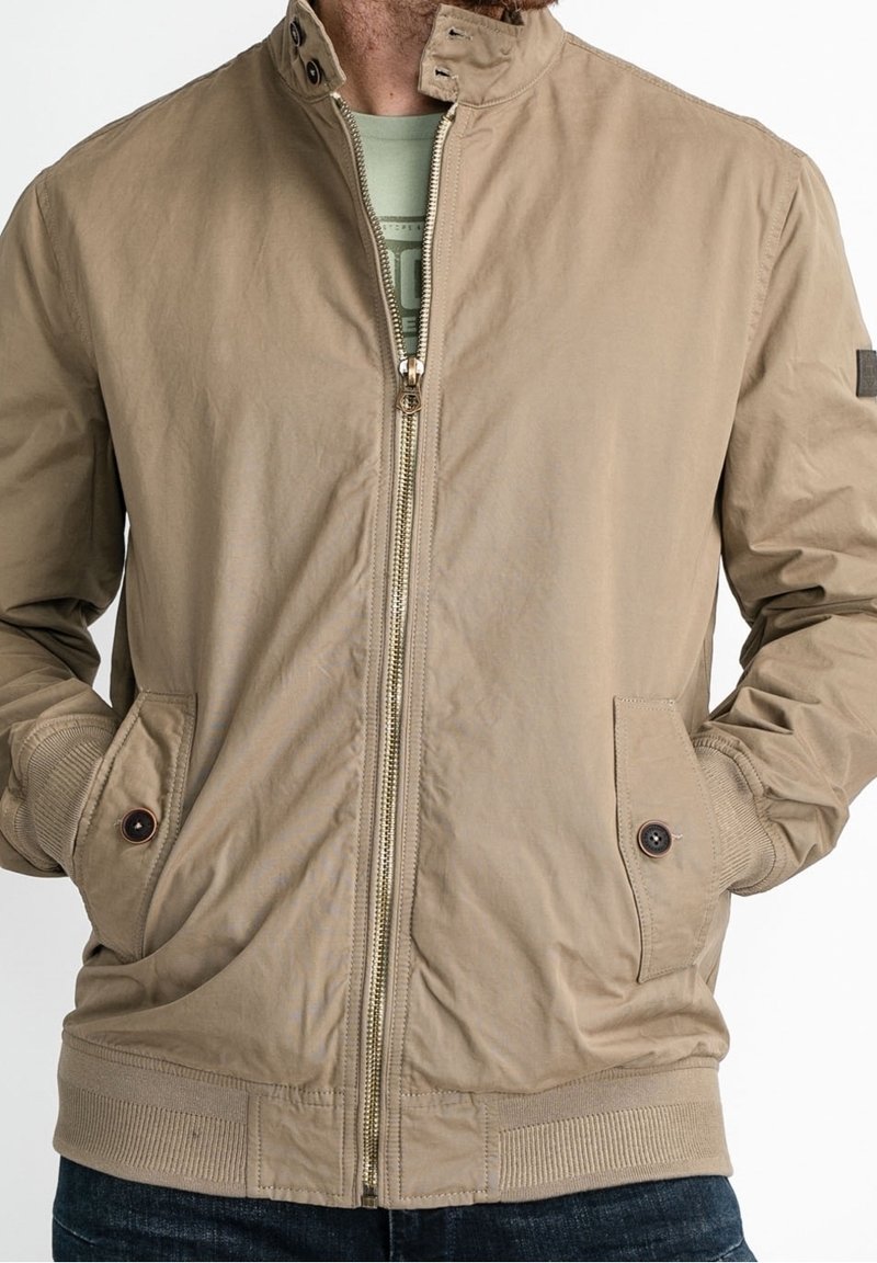 Khaki bomber jacket with a zippered front, ribbed cuffs and hem, two side pockets, and a stand collar. Features smooth, textured fabric.