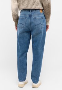 Pantalones vaqueros de tiro alto en azul claro con costuras visibles, dos bolsillos traseros que presentan un diseño decorativo y una etiqueta de cintura de cuero marrón.
