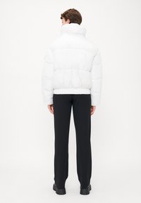 Witte pufferjas met hoge kraag,gevoerd ontwerp, elastische zoom, gecombineerd met zwarte broeken en stevige zwarte schoenen.