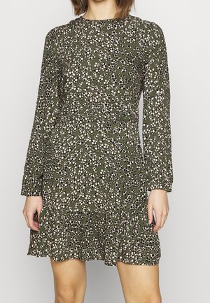 Groen bloemenjurk met lange mouwen, voorzien van een verspreid patroon in wit en zwart, textuurrijk stof en een licht uitlopende zoom.