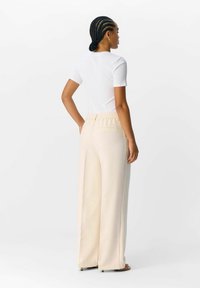 Pantalons wide-leg beige clair avec une taille élastique, associés à un haut ajusté blanc à manches courtes. Tissu lisse et détails minimaux.