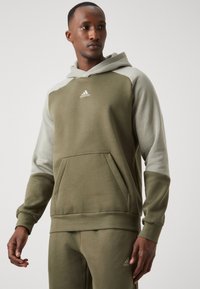 Felpa verde oliva con cappuccio verde chiaro, dotata di tasca a marsupio e del logo Adidas sul petto. Materiale morbido con polsini a coste.