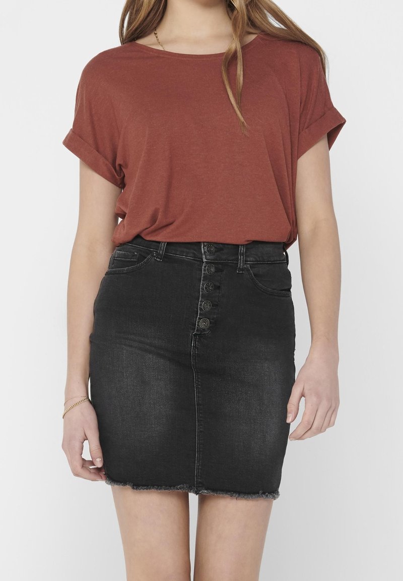 Donna che indossa una maglietta a maniche corte color ruggine infilata in una gonna di jeans nera a vita alta con bottoni frontali e orlo sfrangiato.