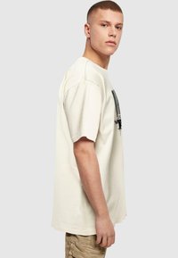 Cremefarvet bomulds-T-shirt med korte ærmer og rund halsudskæring, med et sort grafisk print på fronten. Casual pasform.