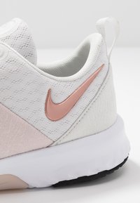 Scarpa sportiva bianca con tomaia in tessuto texturizzato, dettagli rosa chiaro e logo Nike rosa. Presenta una suola intermedia bianca e una suola esterna nera.