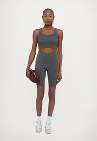 Šedý rebrovaný crop top skombinovaný s vysooko pásovými šortkami, striebornými topánkami a marónovou kabelkou. Jednoduchý dizajn s priliehavým strihom.