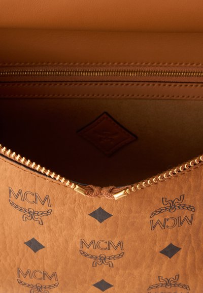 Sac MCM en cuir marron avec fermeture éclair dorée partiellement ouverte, montrant l'intérieur et un motif de logo noir répété sur l'extérieur.