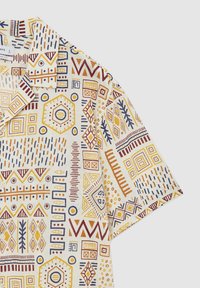 Chemise à manches courtes avec une base crème et divers motifs géométriques en jaune, rouge et bleu. Design avec col et détail de boutons.