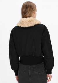Schwarze Bomberjacke mit einem beigen, strukturierten Kunstfellkragen. Verfügt über gerippte Bündchen und einen Bund sowie ein lässiges Passform-Design.