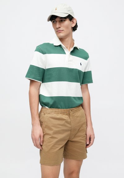 Cămașă polo cu dungi verzi și albe, cu guler, asortată cu pantaloni scurți bej cu talie elastică și buzunare laterale. Șapca completează stilul.