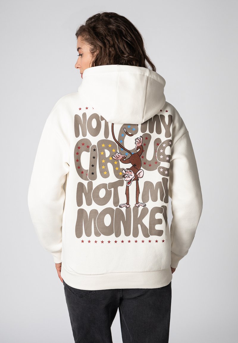 Crème hoodie met een grote grafische afbeelding op de achterkant, voorzien van speelse tekst en een illustratie van een aap, accentueert met gekleurde sterren.