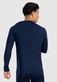 Maglietta sportiva a maniche lunghe di colore blu marina in un tessuto liscio e elasticizzato, con scollo rotondo e design aderente, adatta per attività sportive.