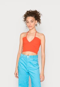 Top cropped halter vermelho com decote em V e design franzido ao centro, combinado com calças largas de corduroy azul claro com cintura alta.