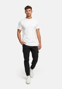 White cotton T-shirt paired with black cargo pants. The outfit is complemented by white sneakers, showcasing a casual design and fit.