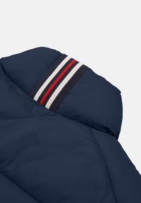 Tamp svart puffjacka med en randig krage i röd, vit och marinblå accent. Slät textur med kviltad design.