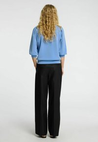 Pūkainu piedurkņu zila blūze un melni platleņķa bikses. Gluda auduma ar brīvu piegriezumu. Blūzei ir ribota apakša un aproču apdare.